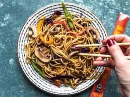 Lo Mein on a plate with someone digging in with chopsticks.