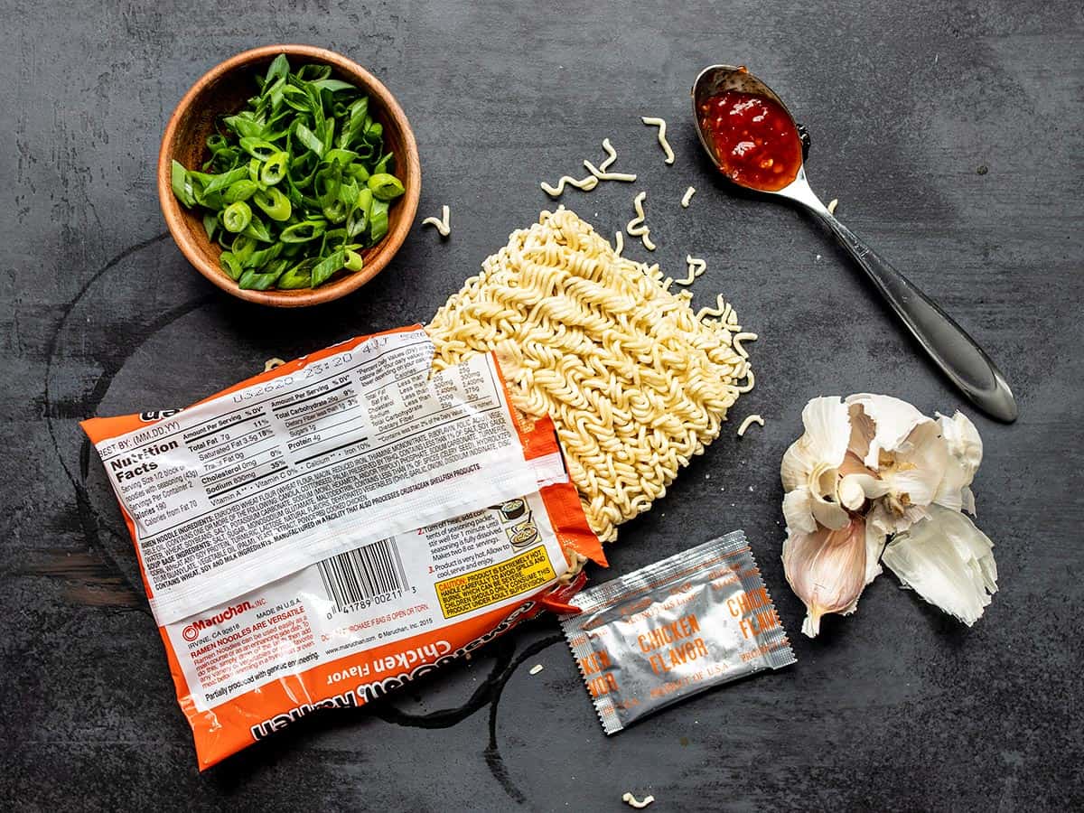 Several ingredients used to make the upgraded instant ramen like chili sauce, uncooked noodles, and green onion. 