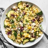 Overhead visning af en skål med forkullet majs og courgette salat med en sort og hvid serviet på siden.