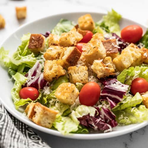 Side view of a shallow bowl with salad topped with homemade croutons.