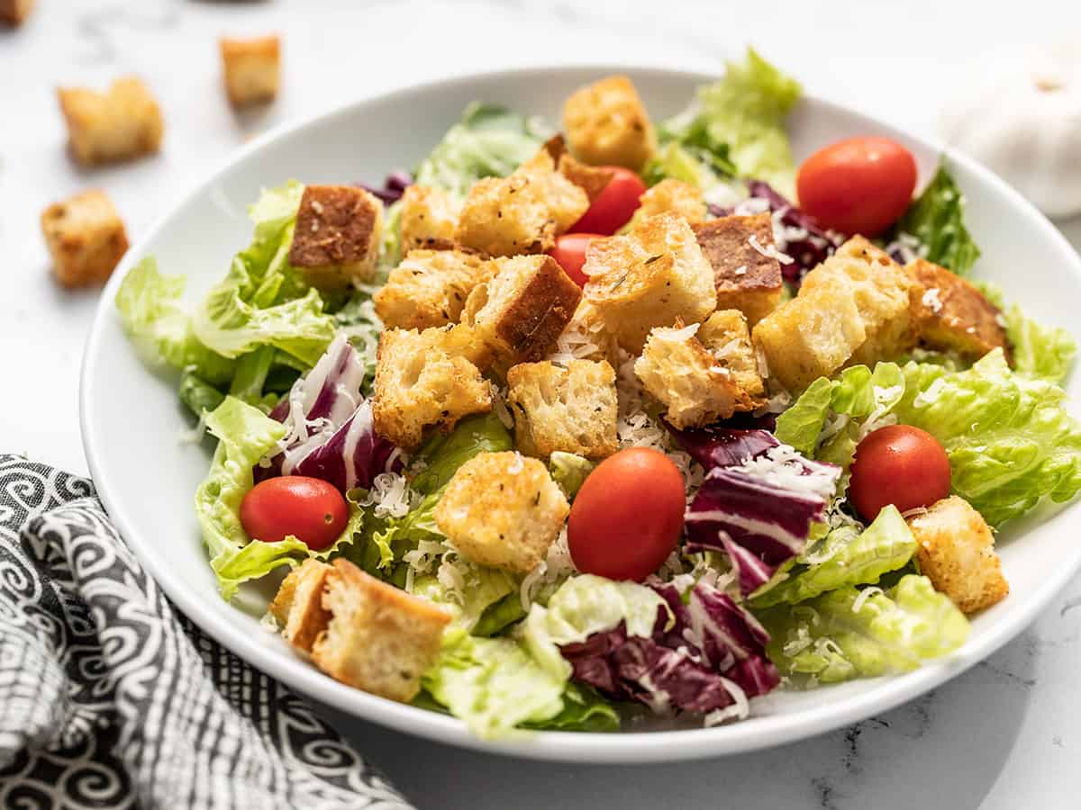 Side view of a shallow bowl with salad topped with homemade croutons.