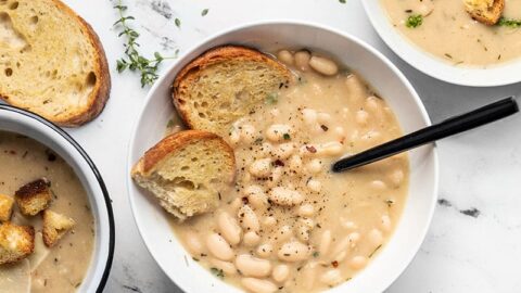 Three bowls of rosemary garlic white bean soup with different toppings (pesto, croutons, Parmesan).