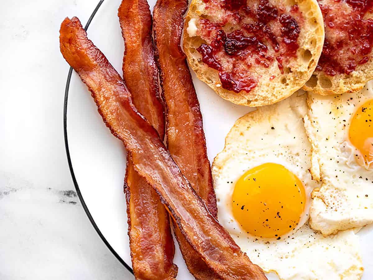 Close up of a plate with oven baked bacon, and egg, and English muffin. 