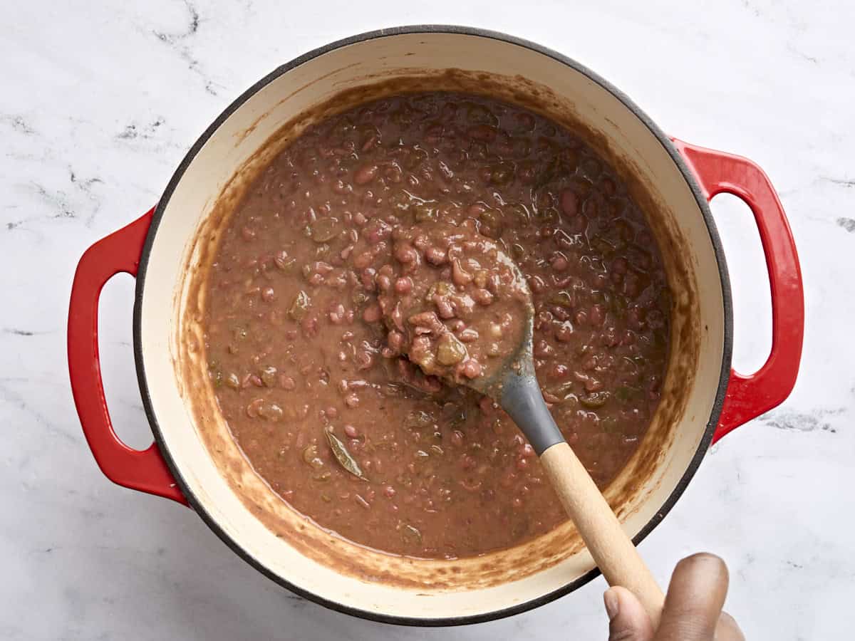 Red beans in a pot with a spoon after being simmered and smashed slightly.