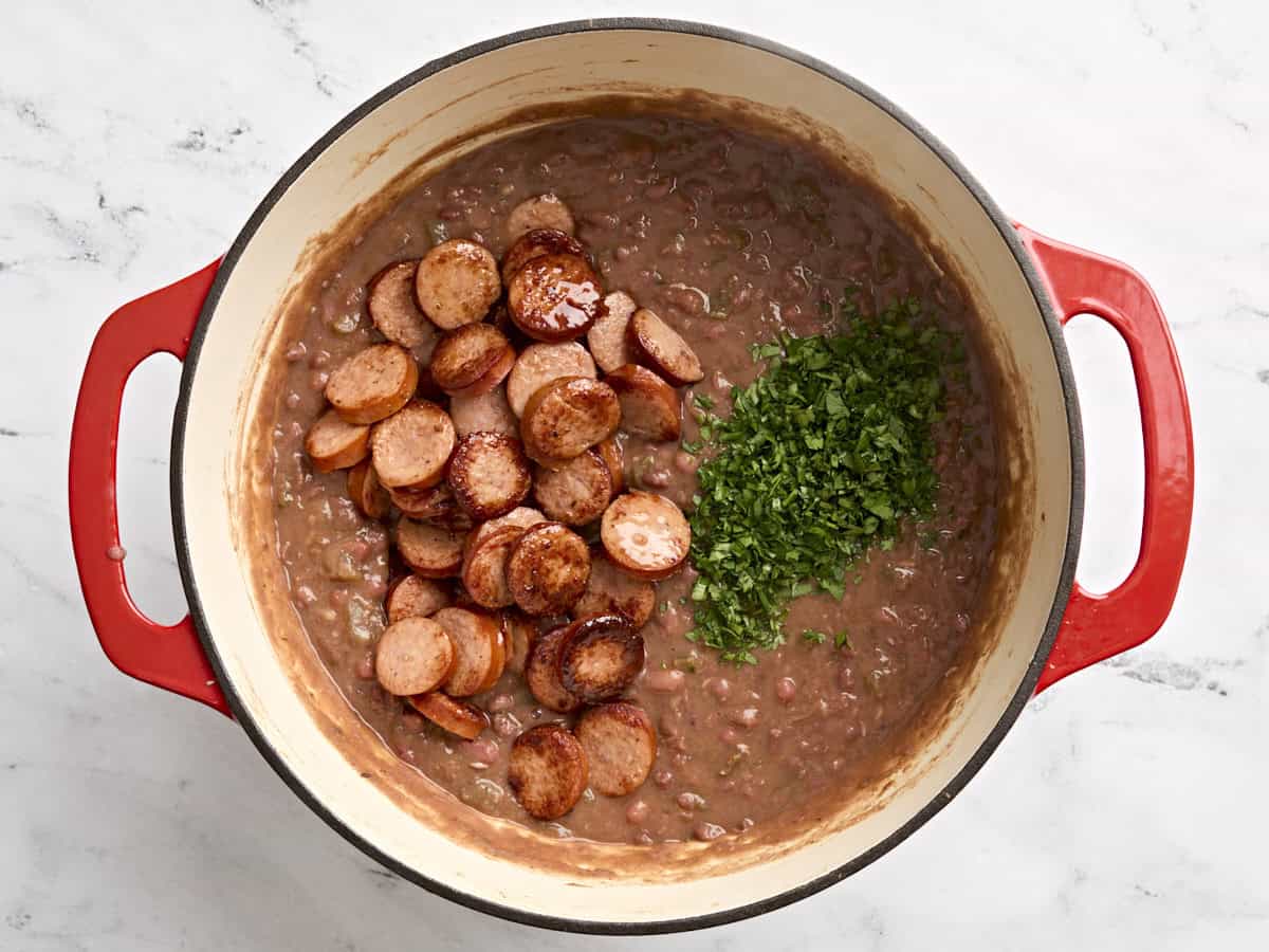 Sliced, cooked sausage and chopped fresh parsley added to a pot of red beans.