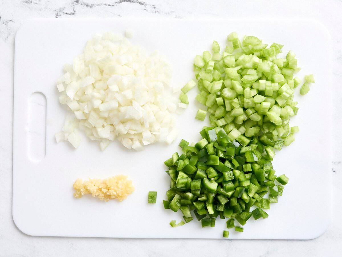 Diced onions, celery, green bell pepper and minced garlic on a cutting board.