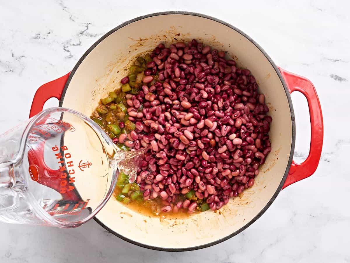 Water being poured into a pot of sauteed veggies and soaked red beans.