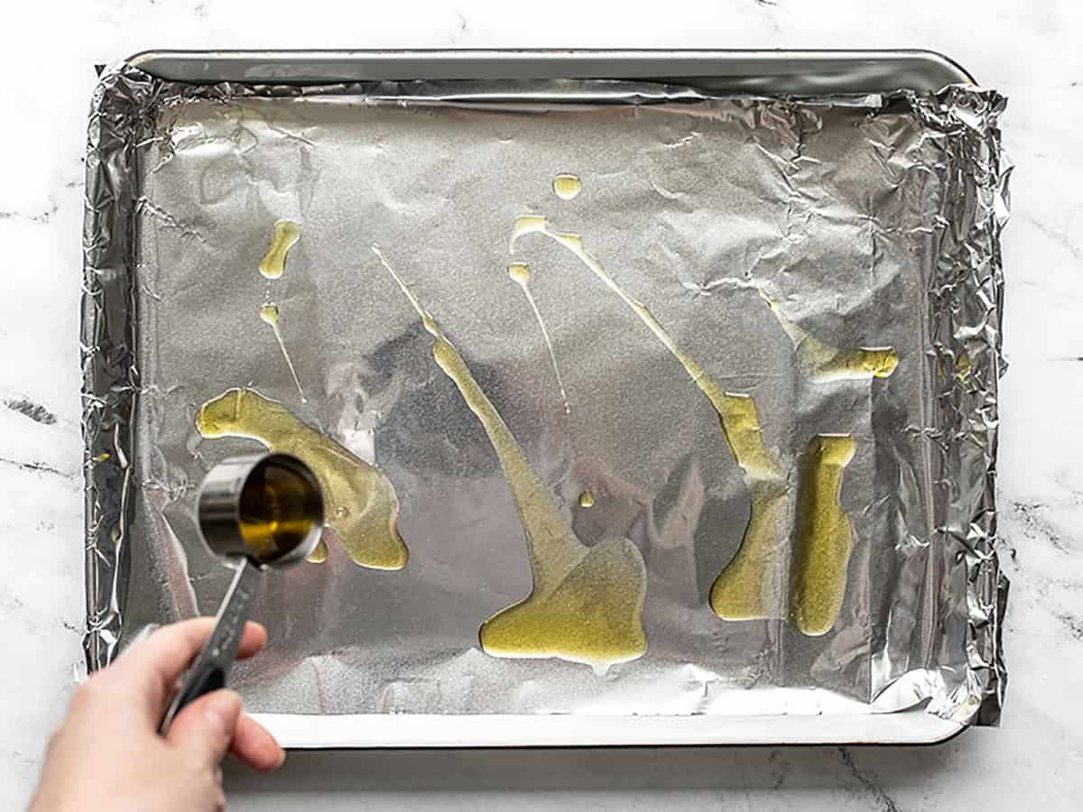 Oil being drizzled onto a foil lined baking sheet. 