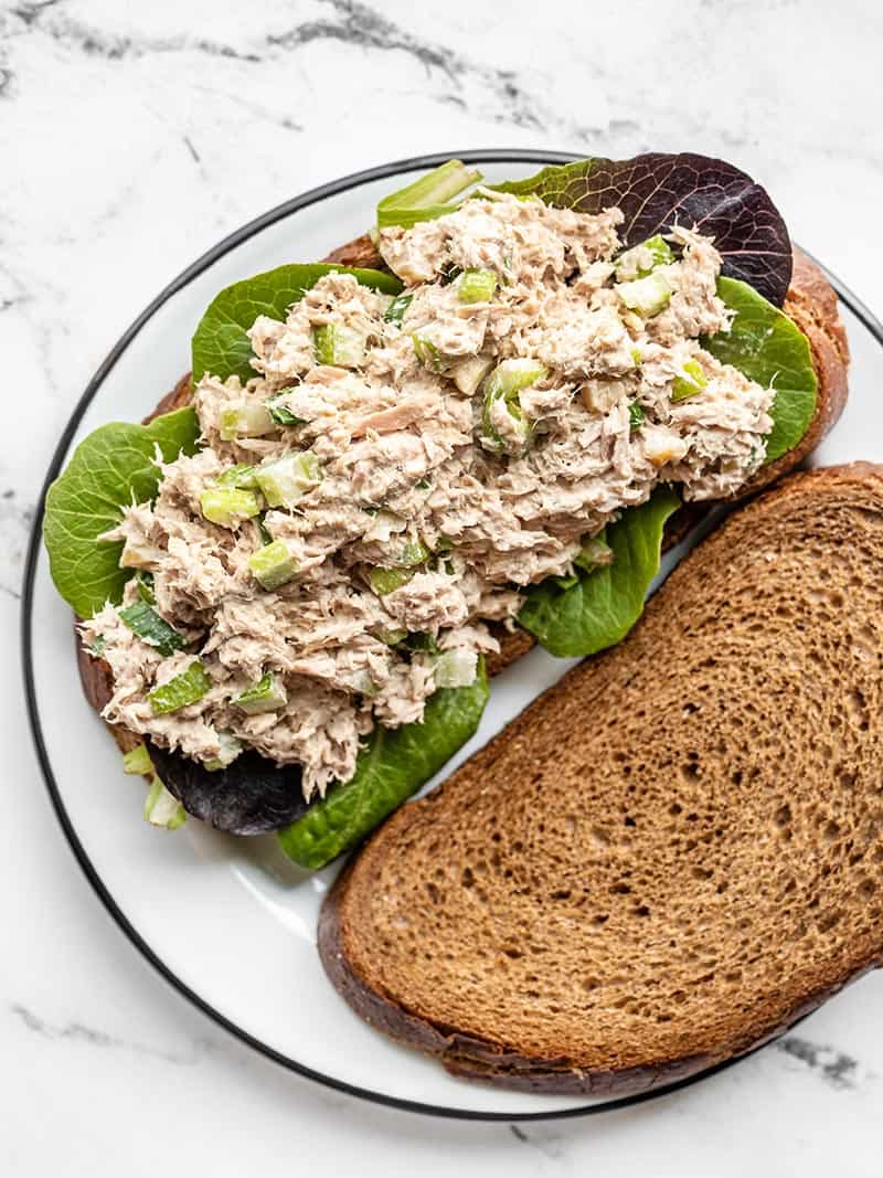 Tuna salad on a piece of bread with baby greens, a second piece of bread on the side.