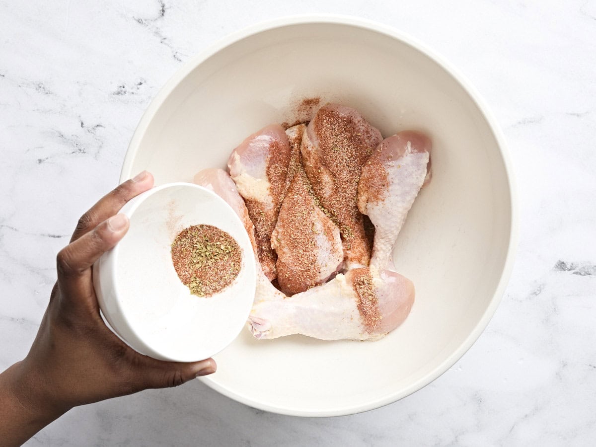 Seasoning mix being poured into a bowl of chicken drumsticks.