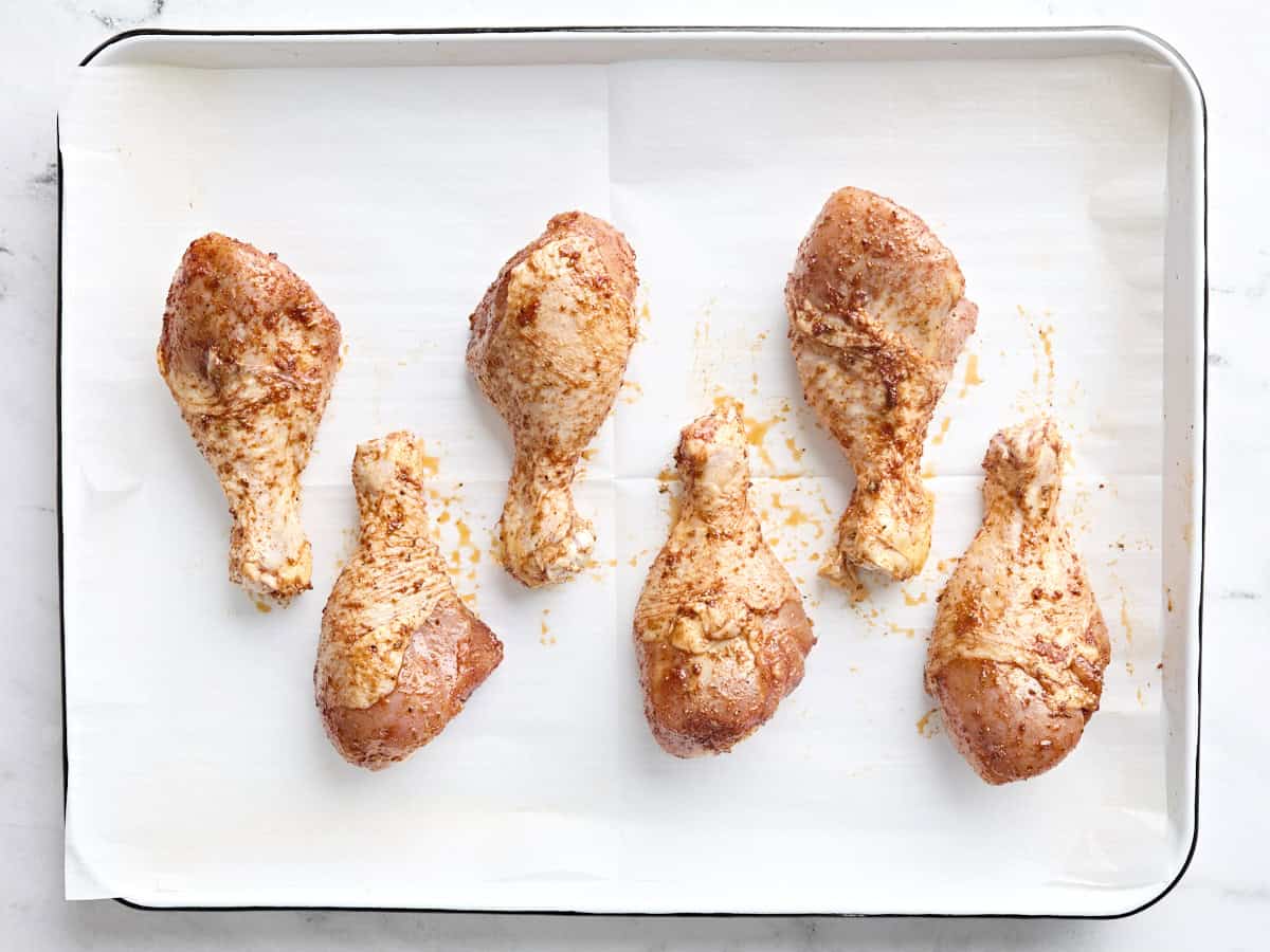 Overhead view of seasoned chicken drumsticks on a parchment lined baking sheet.