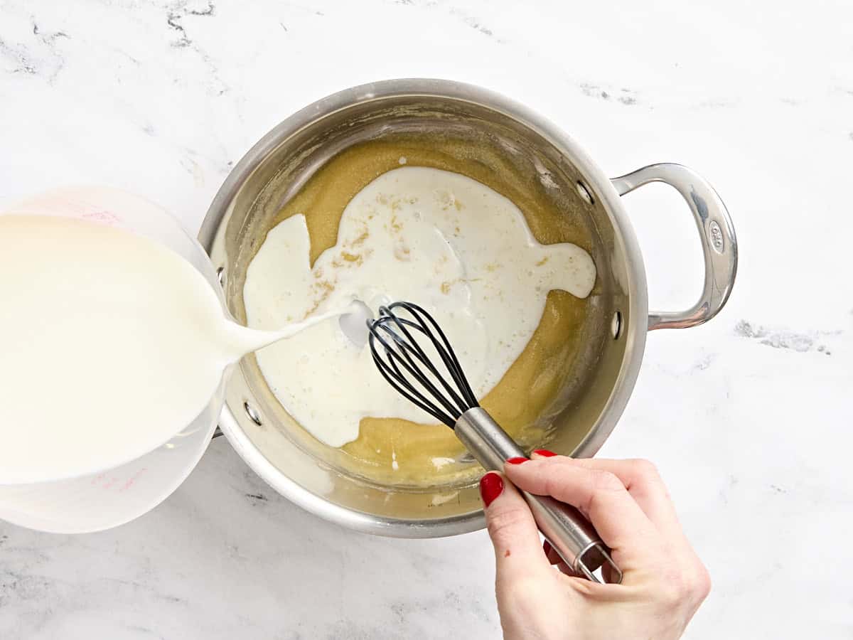 Milk being added to a roux in a pan.