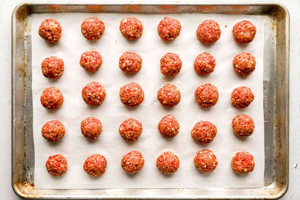 Ground beef and italian seasoning mixture formed into meatballs on a parchment lined baking sheet.