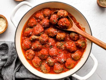 Overhead view of homemade meatballs in a skillet with marinara sauce and a spoon.