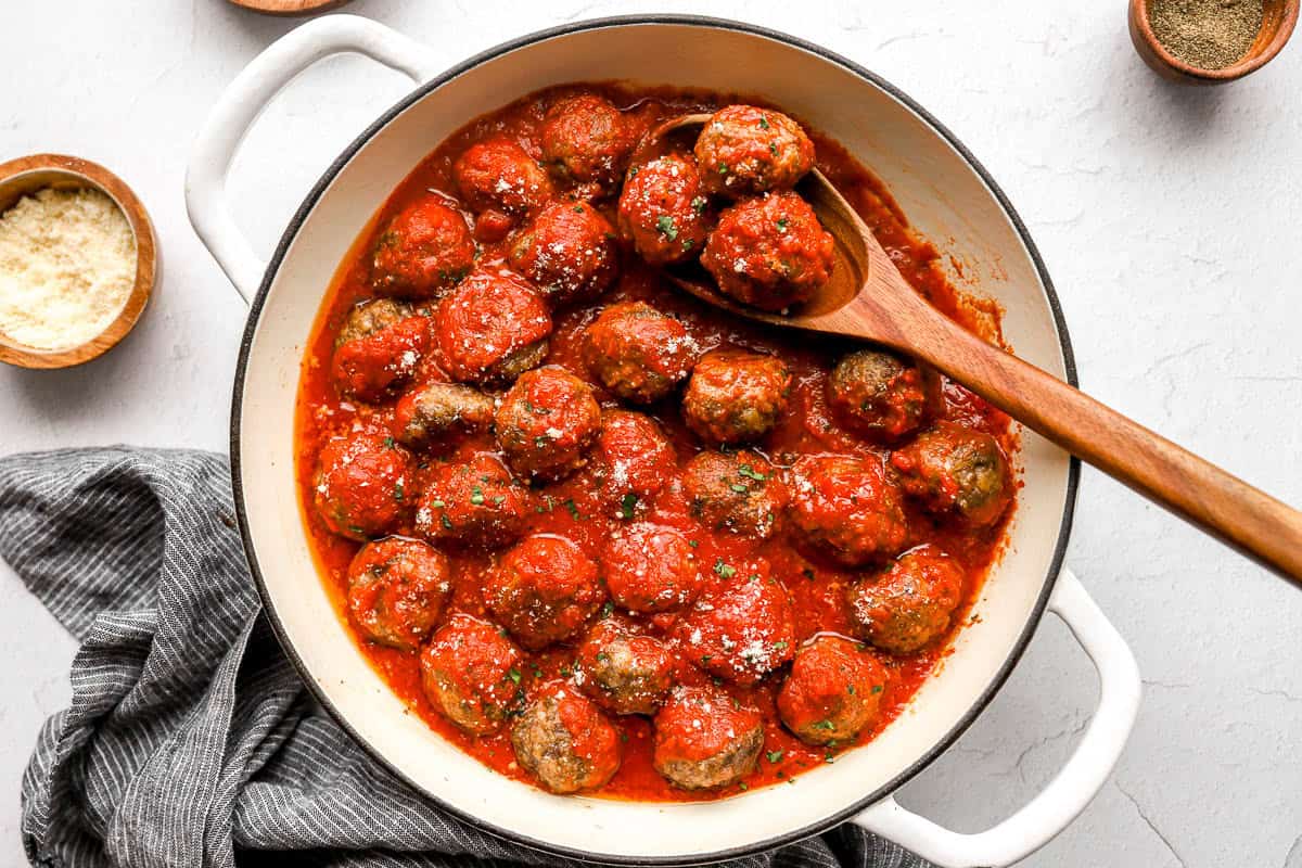 Overhead view of homemade meatballs in a skillet with marinara sauce and a spoon.