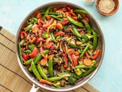 Vegetable stir fry in the skillet against a blue background.