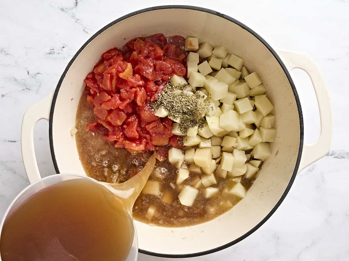 Diced potatoes, diced tomatoes, and beef broth added to a soup pot to make beef vegetable soup.