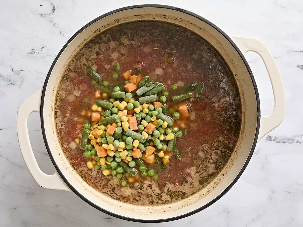 Frozen mixed veggies added to a pot of vegetable beef soup.