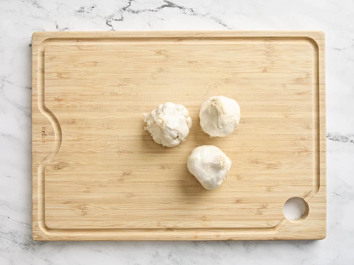 Three heads of garlic on a wooden cutting board.