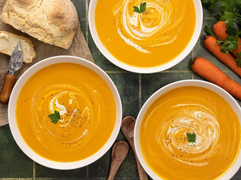 Overhead shot of carrot soup in three white bowls with sour cream swirled in it