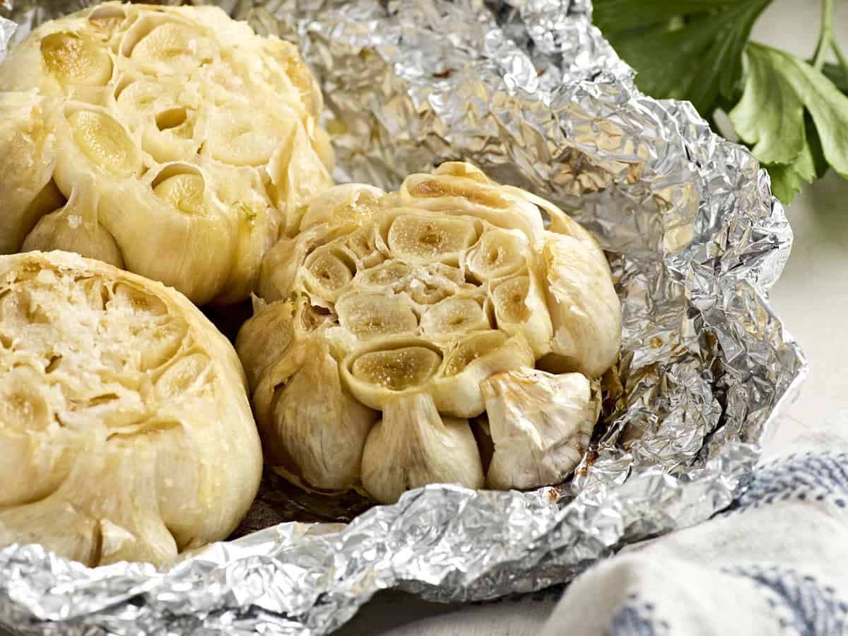 Close up of 3 heads of roasted garlic on a piece of foil.