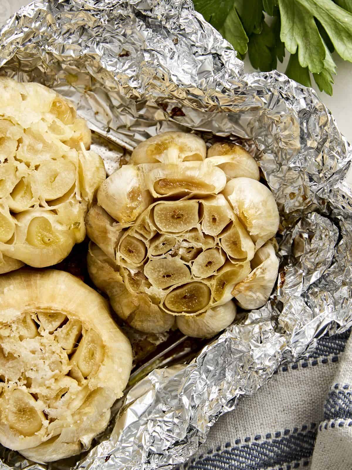 Overhead view of 3 heads of roasted garlic on a piece of foil.