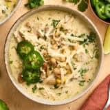 Overhead view of white chili chicken in a bowl, topped with shredded cheese and sliced jalapenos.