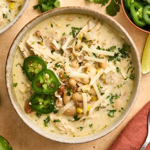 Overhead view of white chili chicken in a bowl, topped with shredded cheese and sliced jalapenos.