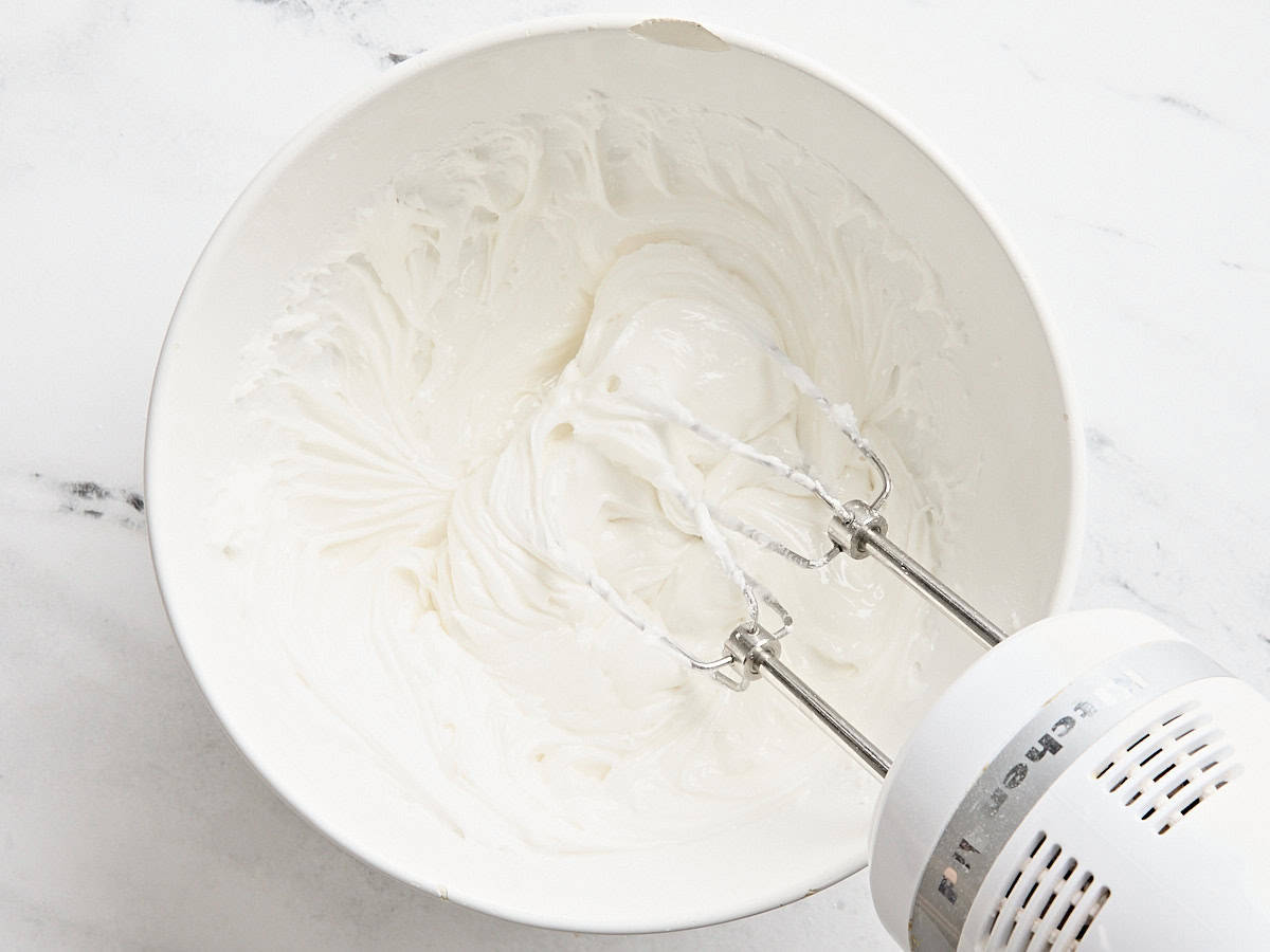 A hand mixer mixing royal icing in a mixing bowl.