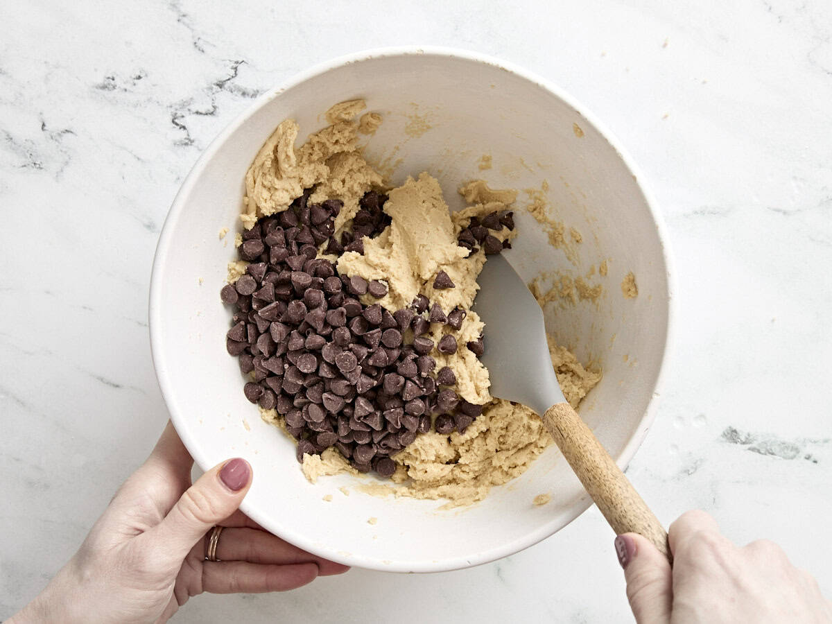 Chocolate chips being folded into chocolate chip cookie dough.