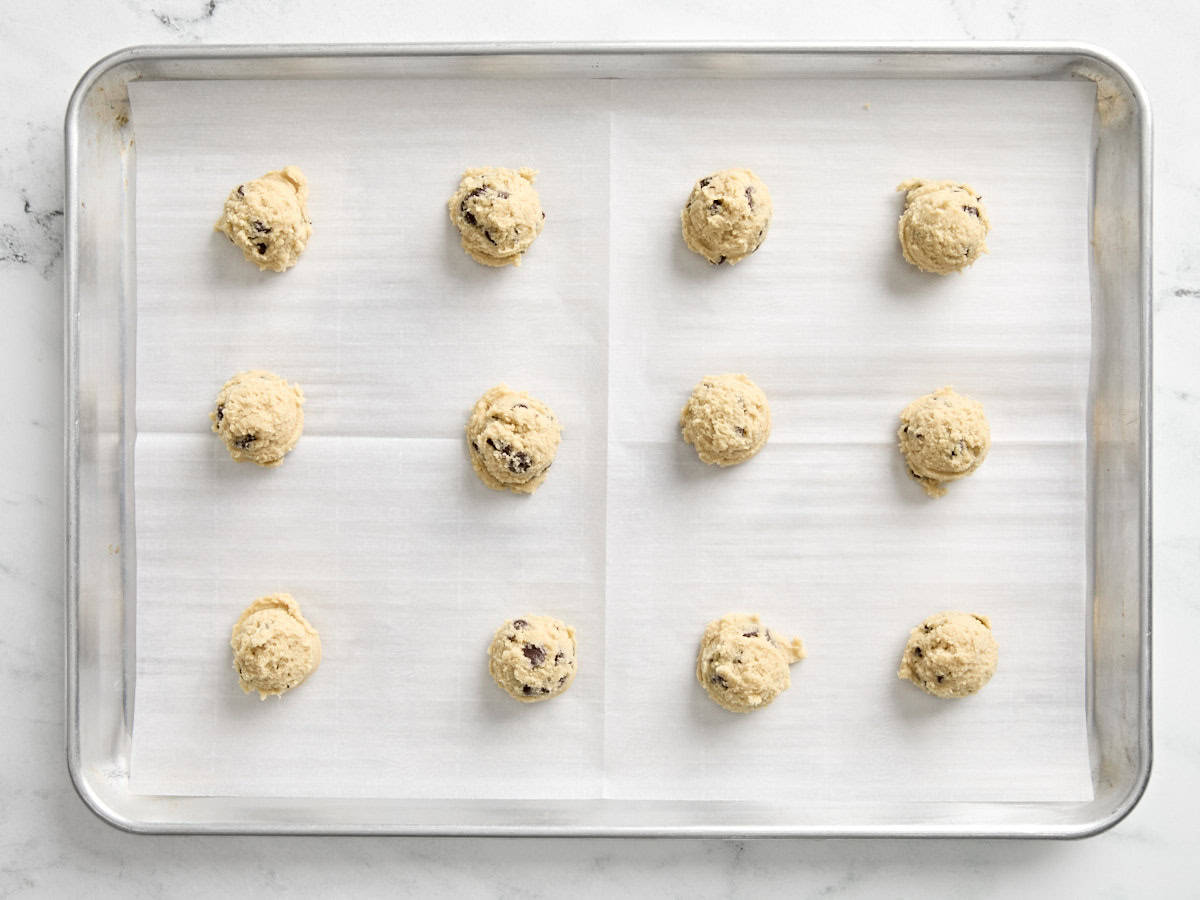 Scooped chocolate chip cookie dough on a parchment lined baking sheet.