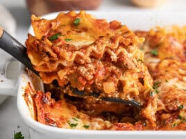 Close up side view of a slice of homemade lasagna being lifted from the casserole dish.