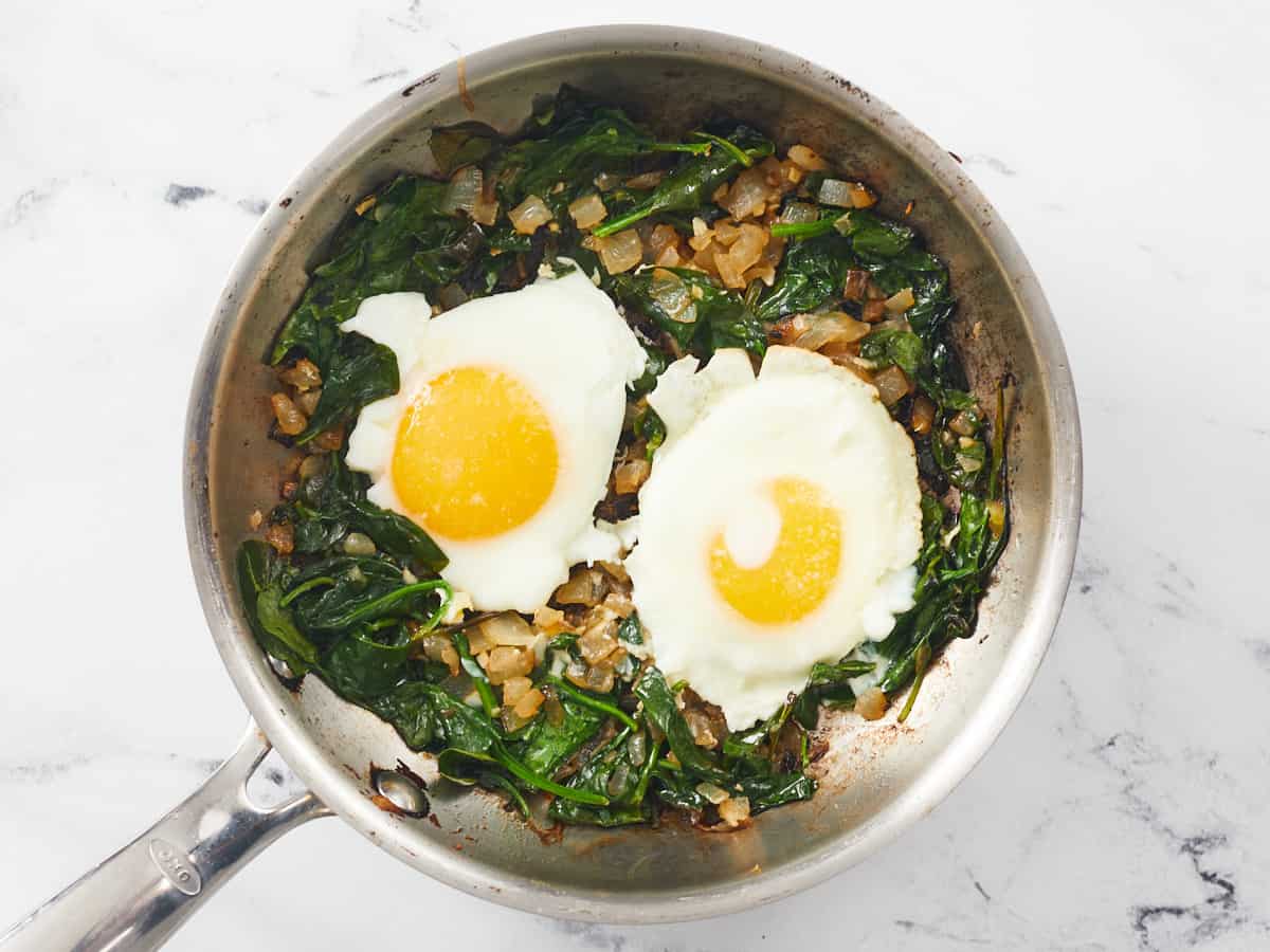 Overhead shot of two sunny-side up eggs cooking in spinach.