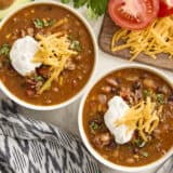 Overhead view of two bowls of taco soup, topped with sour cream and shredded cheese.