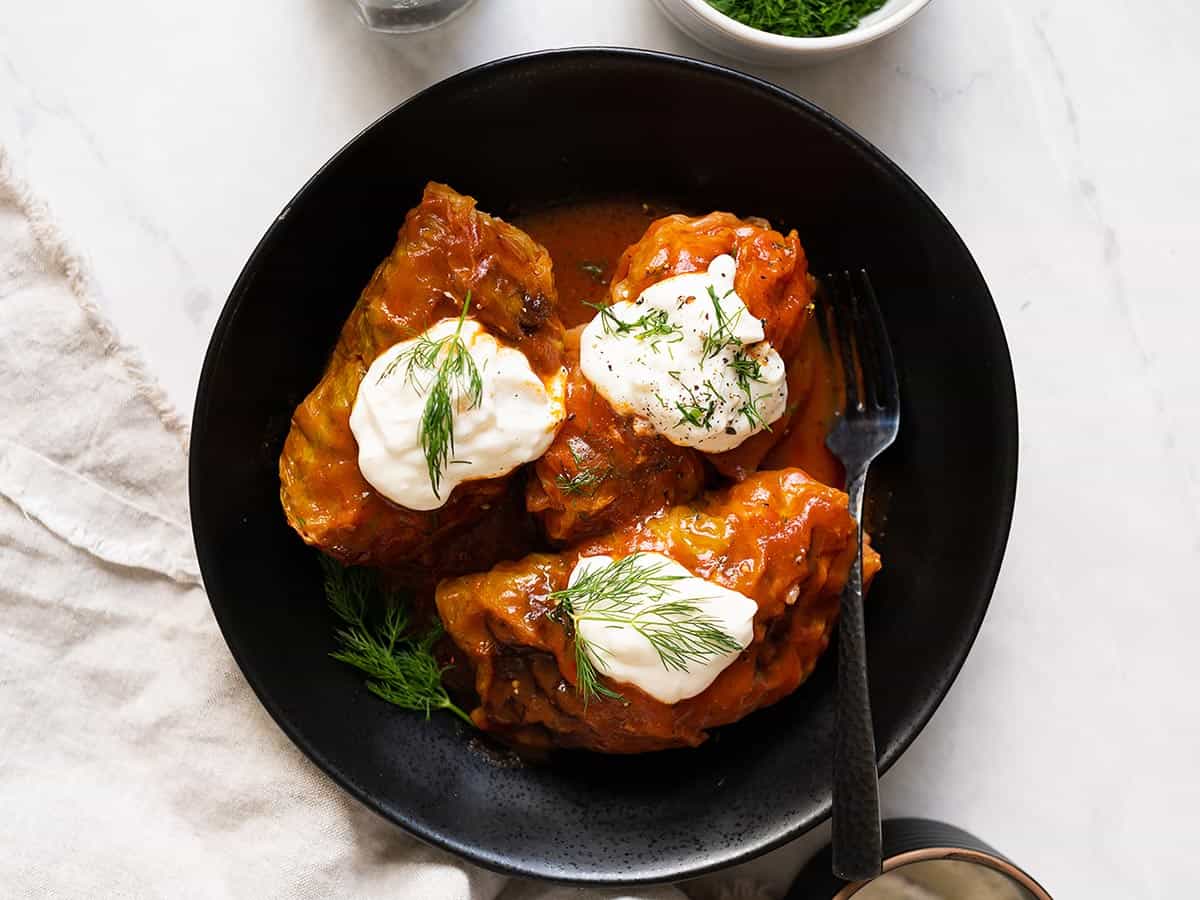 overhead view of cabbage rolls served in a black plate topped with sour cream and fresh dill