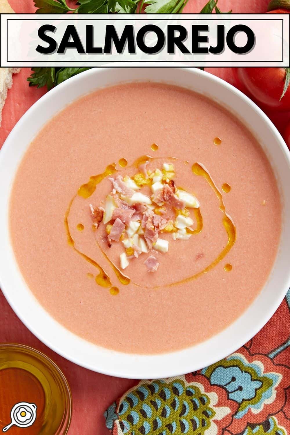 Overhead shot of a white bowl of Salmorejo garnished with a drizzle of olive oil, chopped hard-boiled eggs, and crispy ham crumbles.