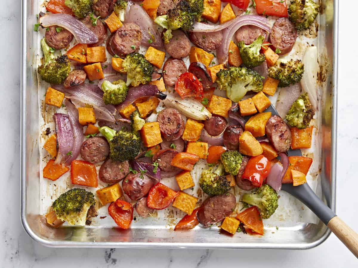 Sheet pan chicken sausage and vegetables dinner with a spatula on the side.