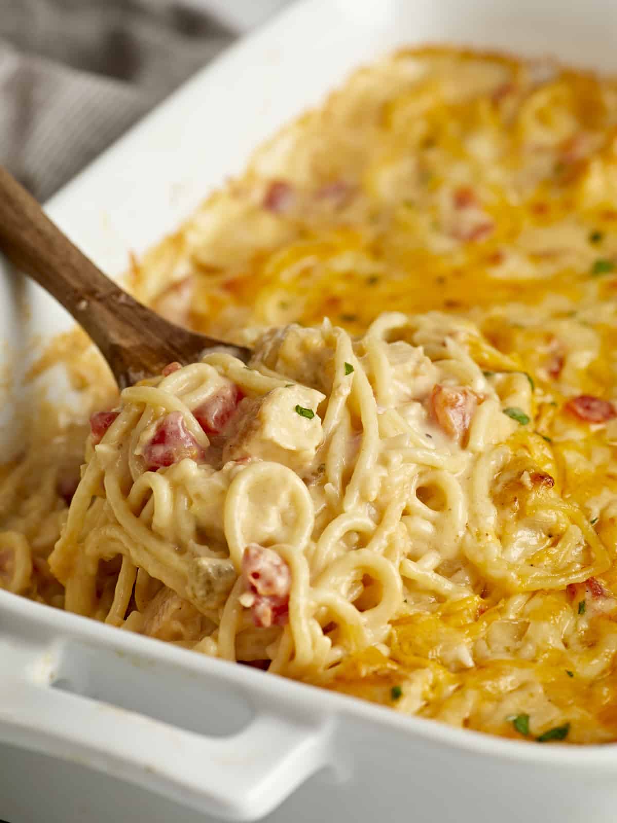 Side close up view of chicken spaghetti in a casserole dish with a wooden spoon lifting some out.