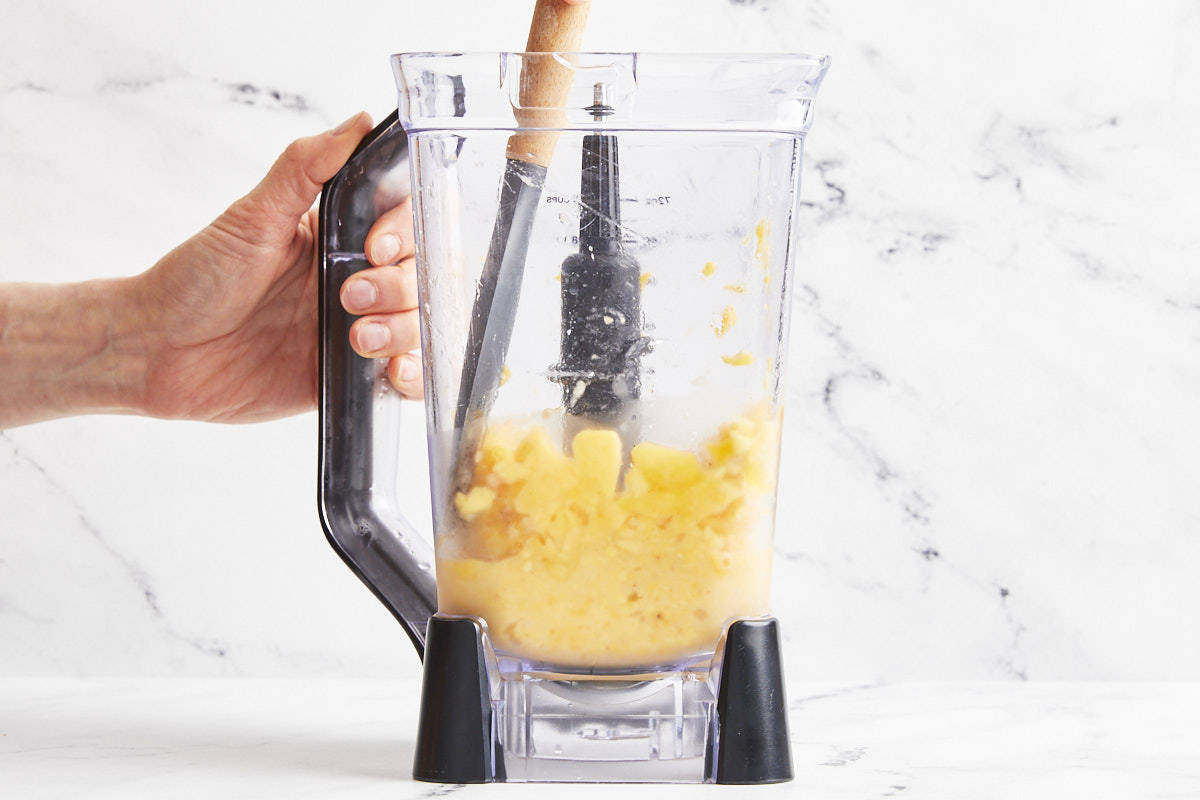 side view of partially blended mango sorbet in a blender with a rubber spatula.