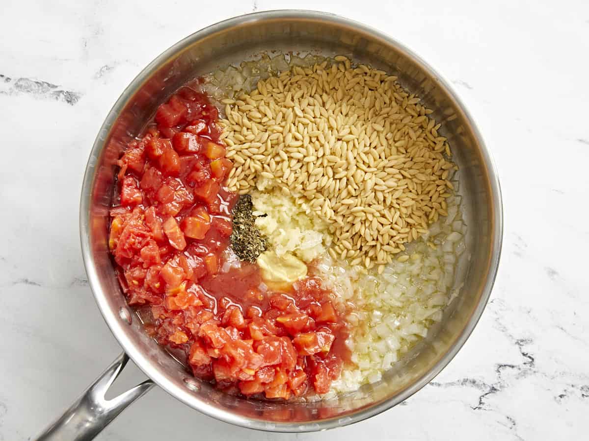 tomatoes and orzo added to sauteed onions in a pan.