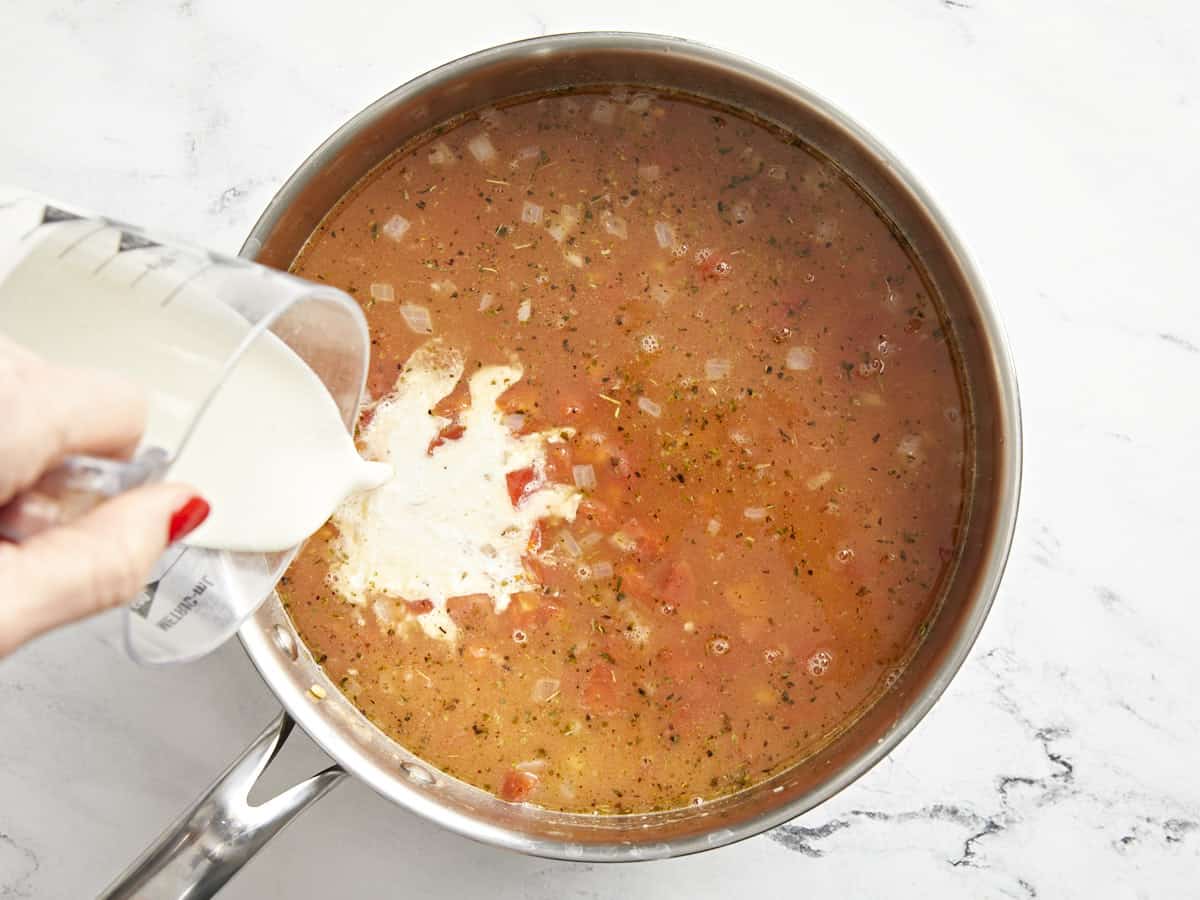 cream poured over tomatoey orzo in a pan.