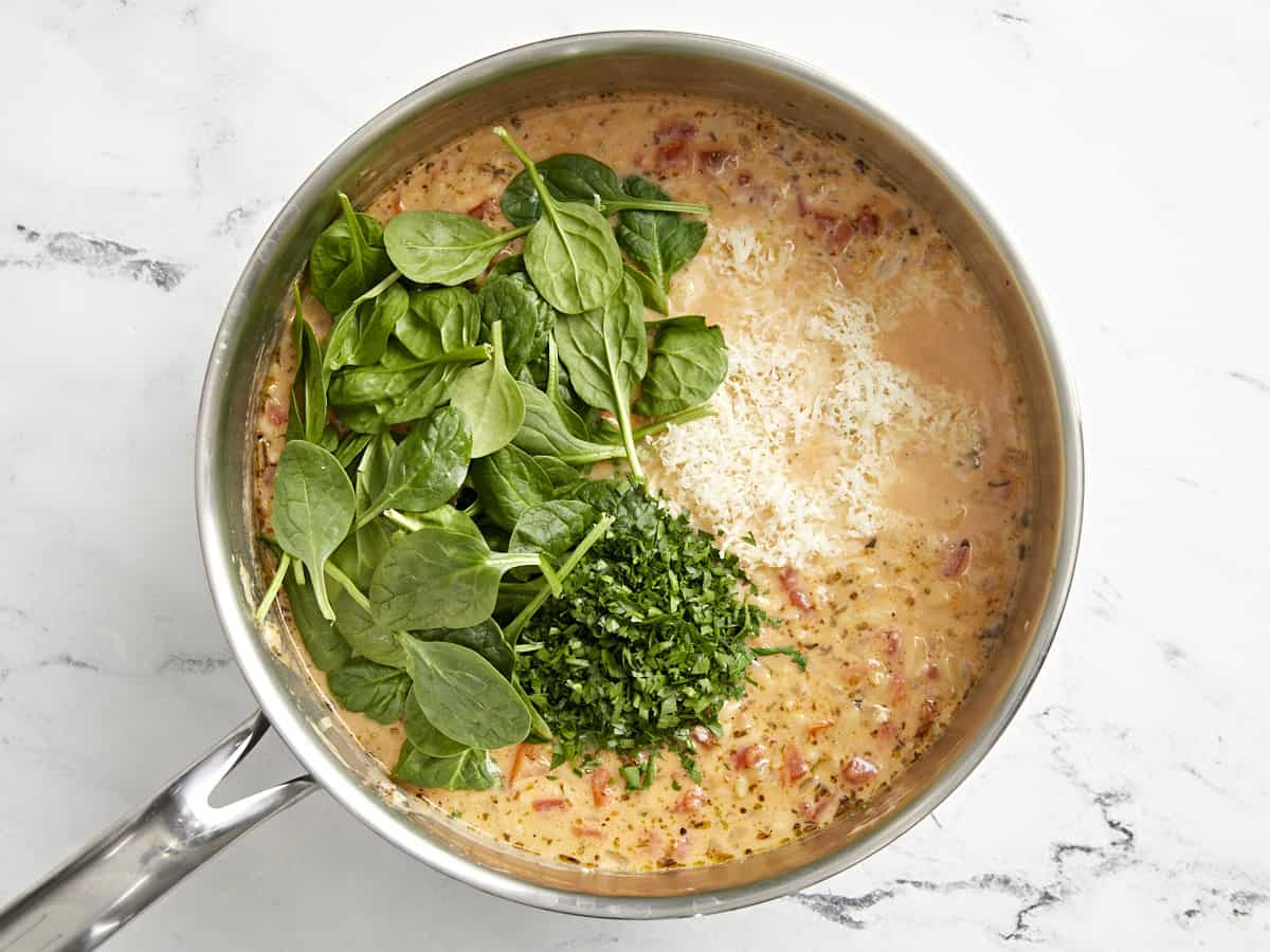 parsley, spinach , and cheese added to creamy tuscan orzo in a pan.