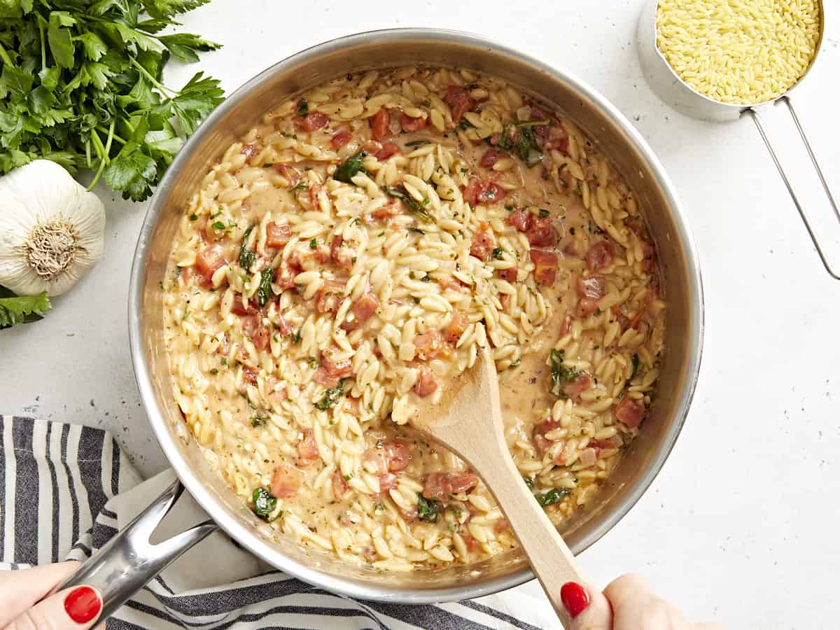 stirring tuscan orzo in a pan with a wooden spoon.