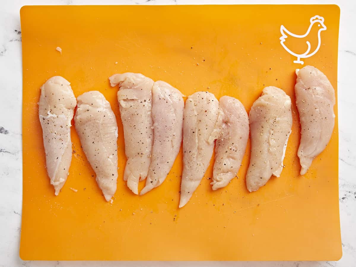 Overhead view of seasoned chicken tenders on a cutting board.