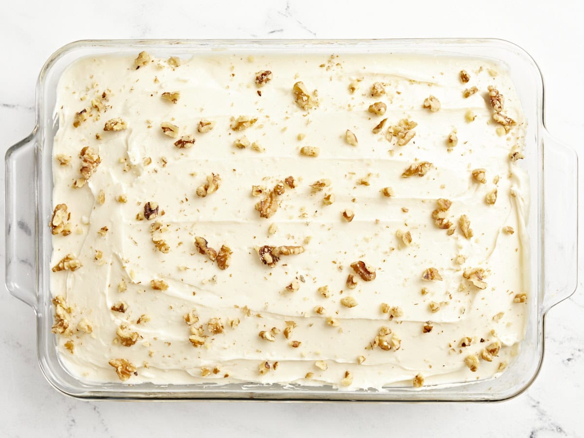 crushed walnuts sprinkled over frosted banana cake in a glass baking dish.