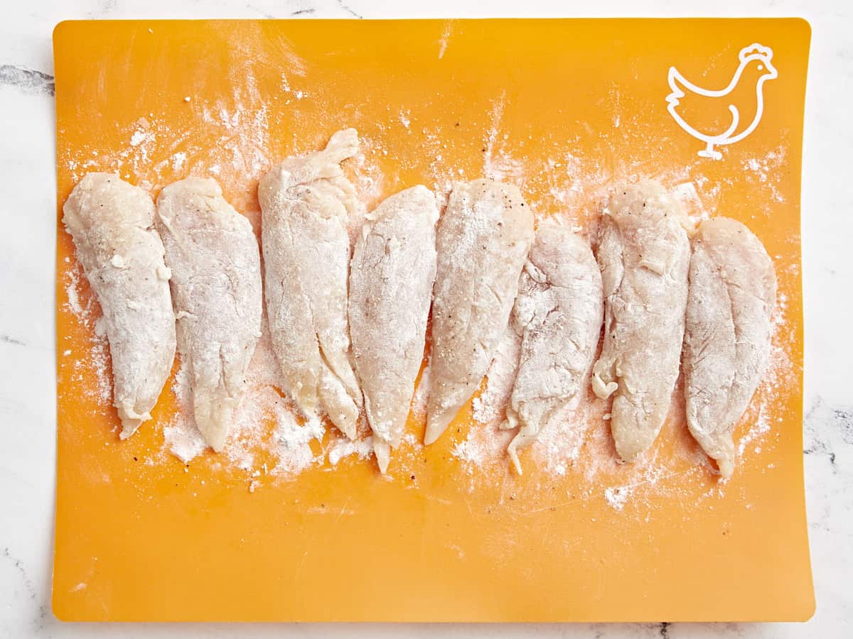 Overhead view of chicken tenders tossed in flour on a cutting board.