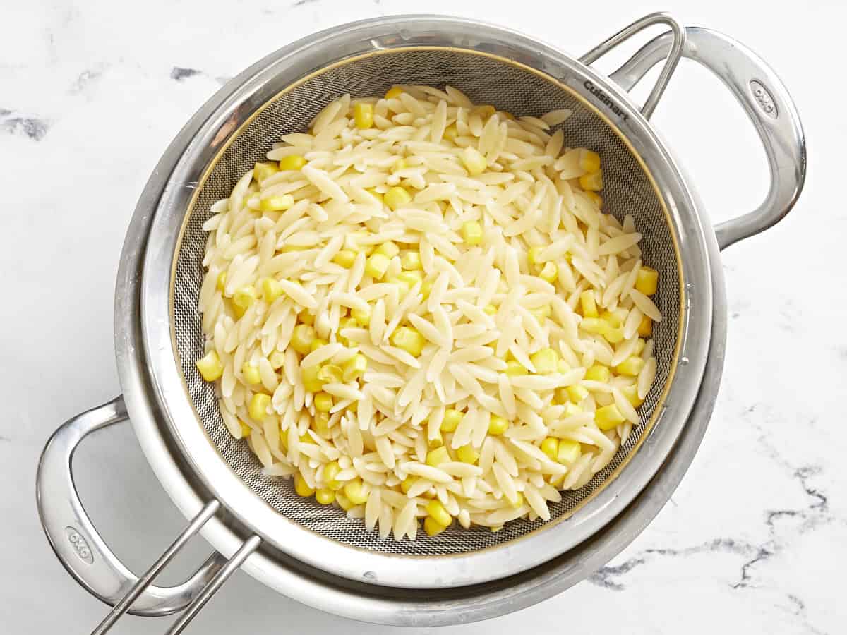Cooked orzo and corn drained in a colander.