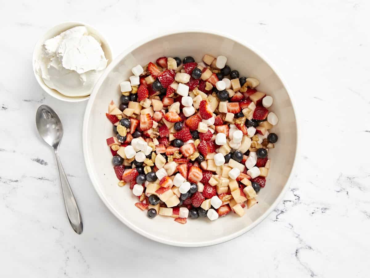 red white and blue fruit salad mixed up in a white bowl with a side of cool whip.