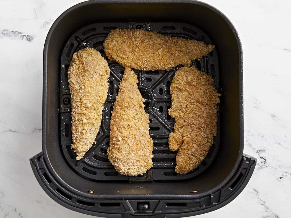 Overhead view of breaded chicken tenders added to air fryer basket.