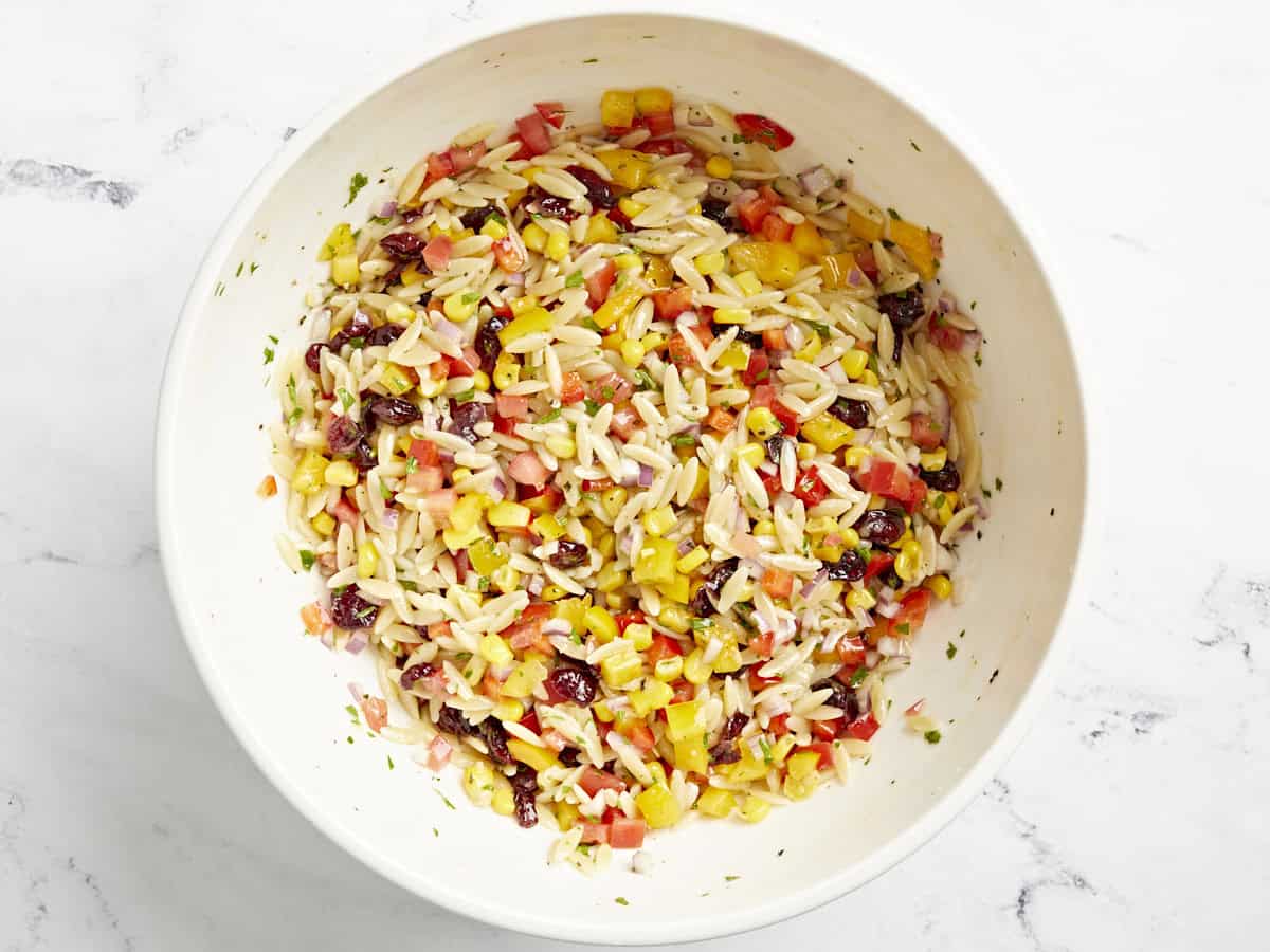 Orzo pasta salad ingredients mixed together in a large bowl.